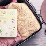 Luggage Bag with pink shirt and orange jersey .Diary with checklist on top of clothes.