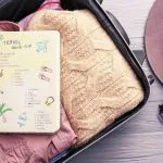 Luggage Bag with pink shirt and orange jersey .Diary with checklist on top of clothes.
