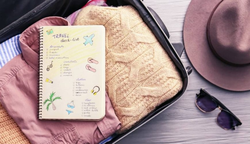 Luggage Bag with pink shirt and orange jersey .Diary with checklist on top of clothes.