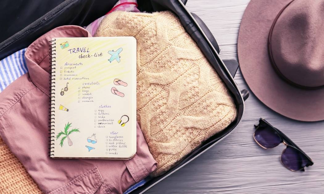 Luggage Bag with pink shirt and orange jersey .Diary with checklist on top of clothes.