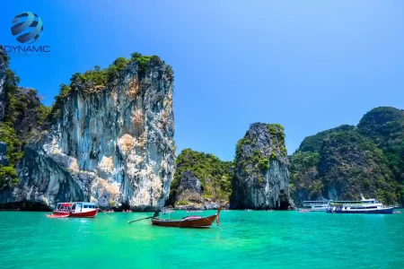 Turquoise waters with limestone cliffs and traditional long‑tail boats under a bright sunny sky at a popular Thailand Phuket island destination