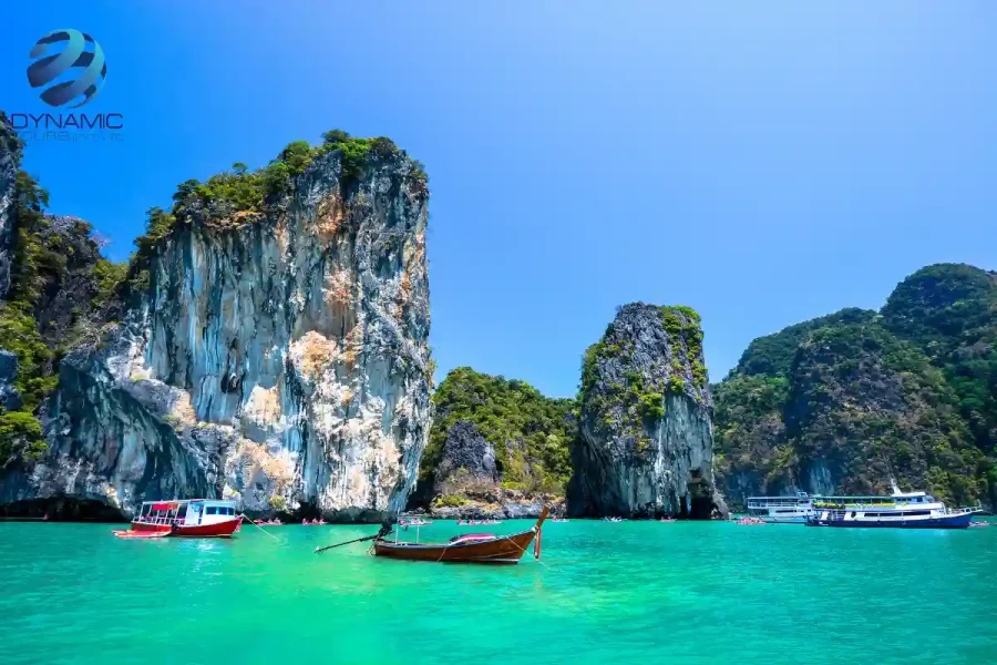 Turquoise waters with limestone cliffs and traditional long‑tail boats under a bright sunny sky at a popular Thailand Phuket island destination