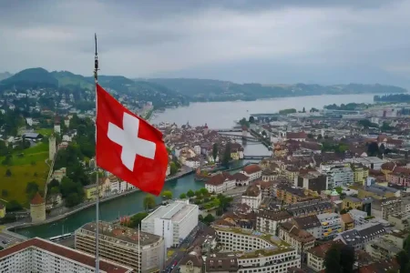 Travel poster featuring aerial view of Swiss city with large Swiss flag, river bridges, traditional European architecture, and mountain backdrop